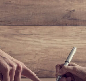 male hand pointing to a piece of paper while other person signs it